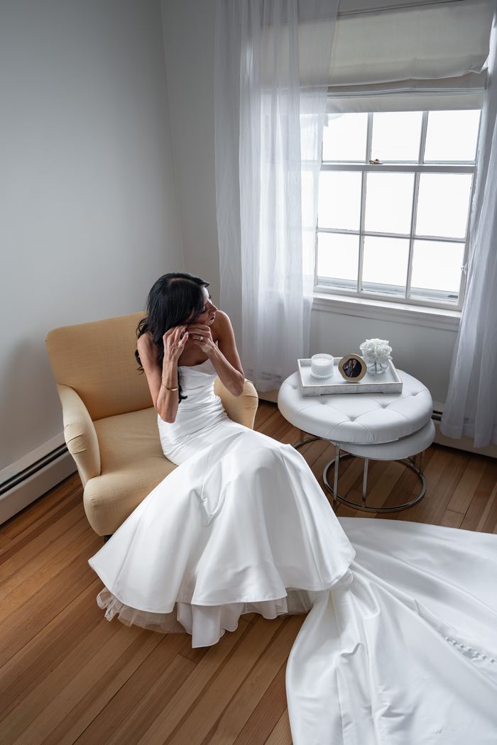 Bride fixing an earring by a bright window